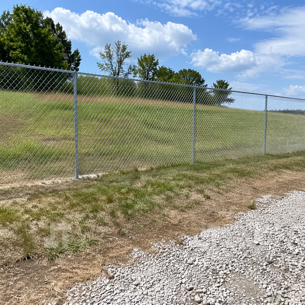 Chain-Link Fence – Galvanised steel mesh fence installed along sloped grassy boundary - Sample Image